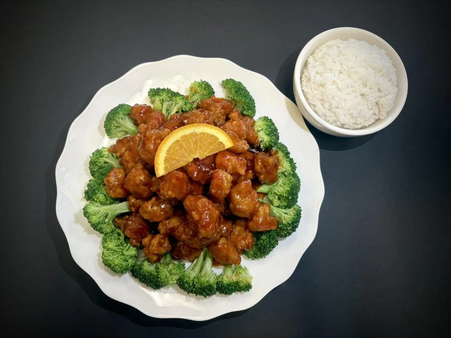 Orange glazed chicken chunks garnished with broccoli and orange slice with side rice at Lucky House, a Chinese restaurant in Surprise Orange glazed chicken chunks garnished with broccoli and orange slice with side rice at Lucky House, a Chinese restaurant in Surprise